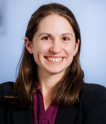 A professional headshot of Tamara L. Slater, smiling and wearing a black blazer on a blue background