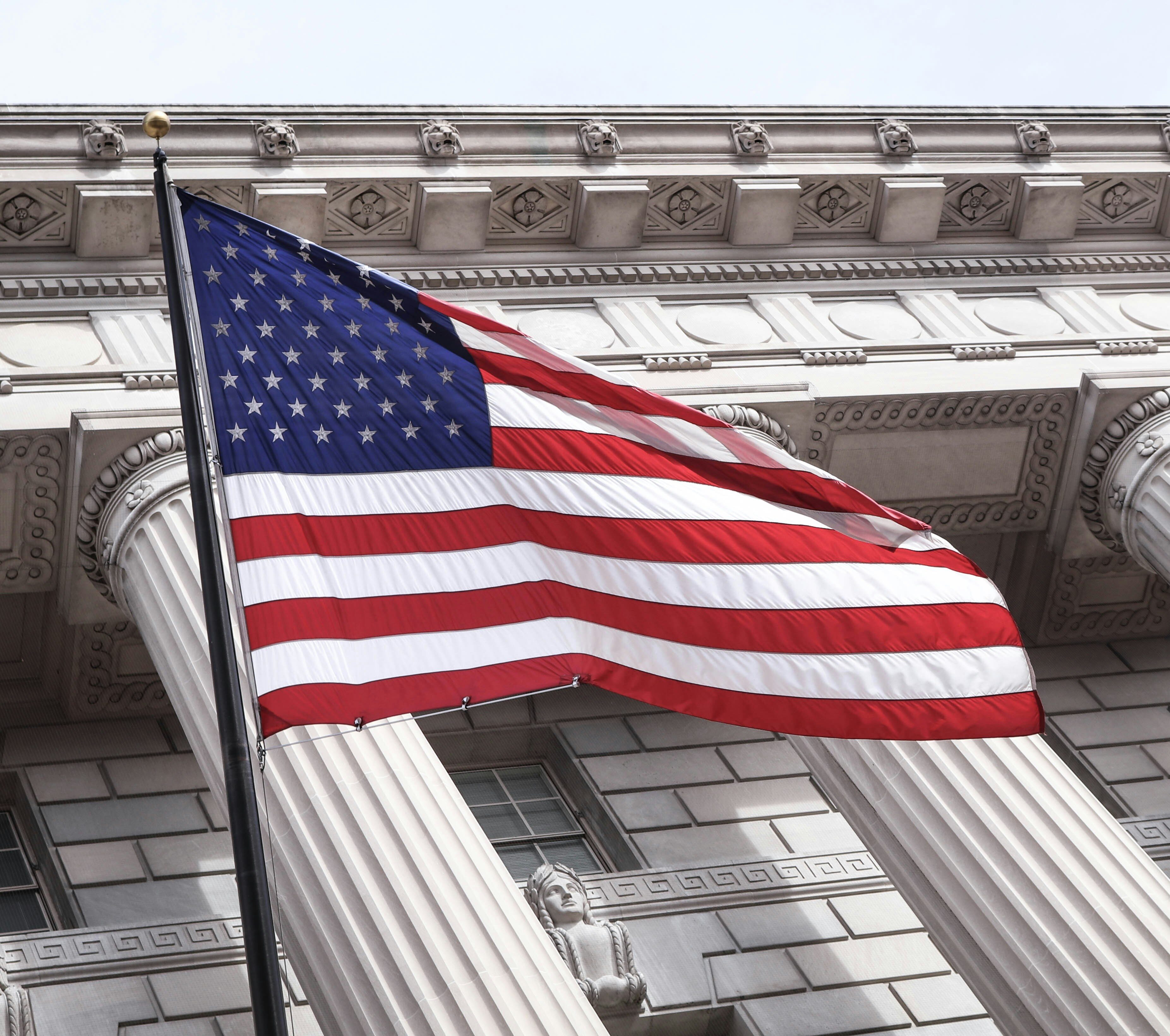 An American flag waving in front of a classical government building with large stone columns.